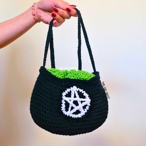 K&ouml;nnte beinhalten: Eine schwarze geh&auml;kelte Tasche mit einem wei&szlig;en Pentagramm-Design. Die Tasche hat ein gr&uuml;nes Futter und zwei schwarze Henkel.