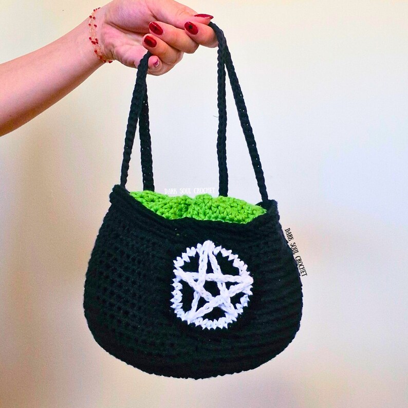 K&ouml;nnte beinhalten: Eine schwarze geh&auml;kelte Tasche mit einem wei&szlig;en Pentagramm-Design. Die Tasche hat ein gr&uuml;nes Futter und zwei schwarze Henkel.