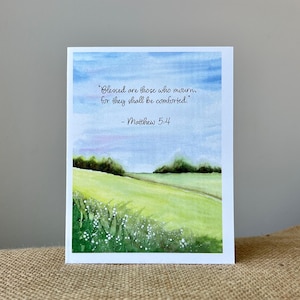 May include: A watercolor greeting card featuring a landscape scene with a green field, blue sky, and the text "Blessed are those who mourn, for they shall be comforted." - Matthew 5:4.