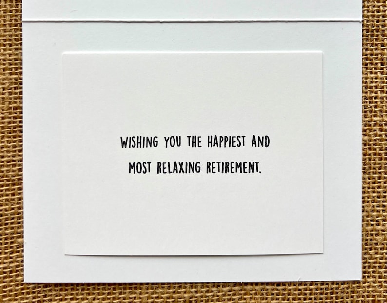 May include: A white greeting card with the message "WISHING YOU THE HAPPIEST AND MOST RELAXING RETIREMENT" in black text. The card is set against a textured, neutral-toned background.