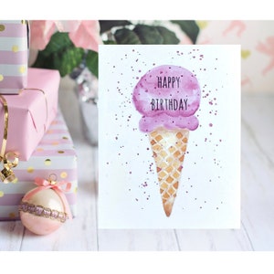 May include: A watercolor birthday card featuring a purple ice cream cone with the words "Happy Birthday" in black. The cone is a light brown color. The background is white with purple paint splatters.