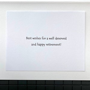 May include: A white greeting card with the message "Best wishes for a well deserved and happy retirement!" in black text. The card is set against a white border and a black tiled background.