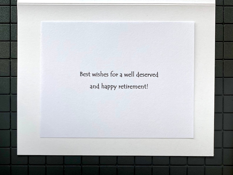 May include: A white greeting card with the message "Best wishes for a well deserved and happy retirement!" in black text. The card is set against a white border and a black tiled background.