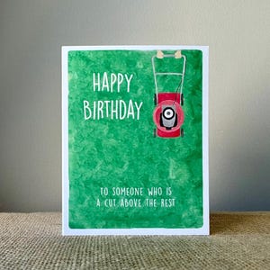 May include: A birthday greeting card with a green background and white border. The card features the words "HAPPY BIRTHDAY" in white, along with a red lawnmower illustration. The text "TO SOMEONE WHO IS A CUT ABOVE THE REST" is also included.