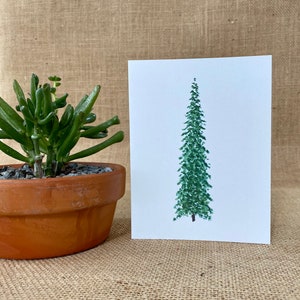 May include: A white greeting card featuring a centered, vertical watercolor illustration of a tall, slender evergreen tree in shades of dark and forest green. The tree has a pointed top and a visible brown trunk at the base of the illustration.