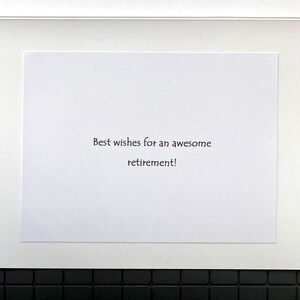 May include: A white greeting card with the message "Best wishes for an awesome retirement!" printed in black. The card is set against a white mat and a black tiled background.