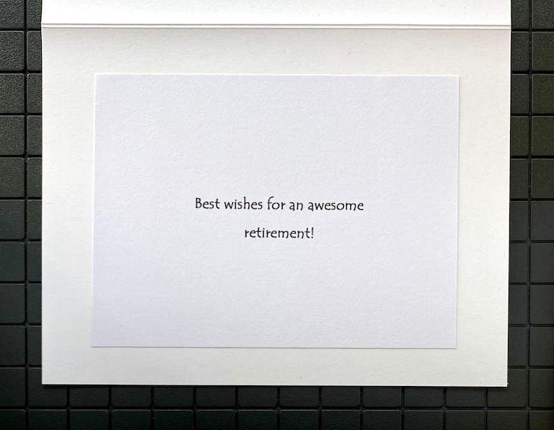 May include: A white greeting card with the message "Best wishes for an awesome retirement!" printed in black. The card is set against a white mat and a black tiled background.