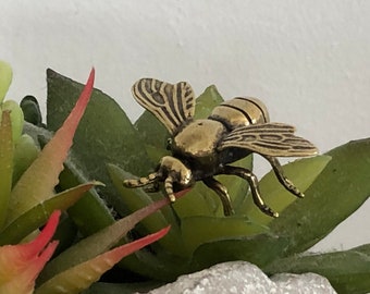 May include: A gold-colored metal bee figurine with detailed wings and legs, perched on a green succulent plant.