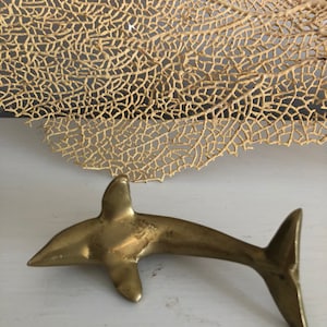 May include: A gold-colored metal dolphin figurine. The dolphin is in a swimming pose with its tail raised.