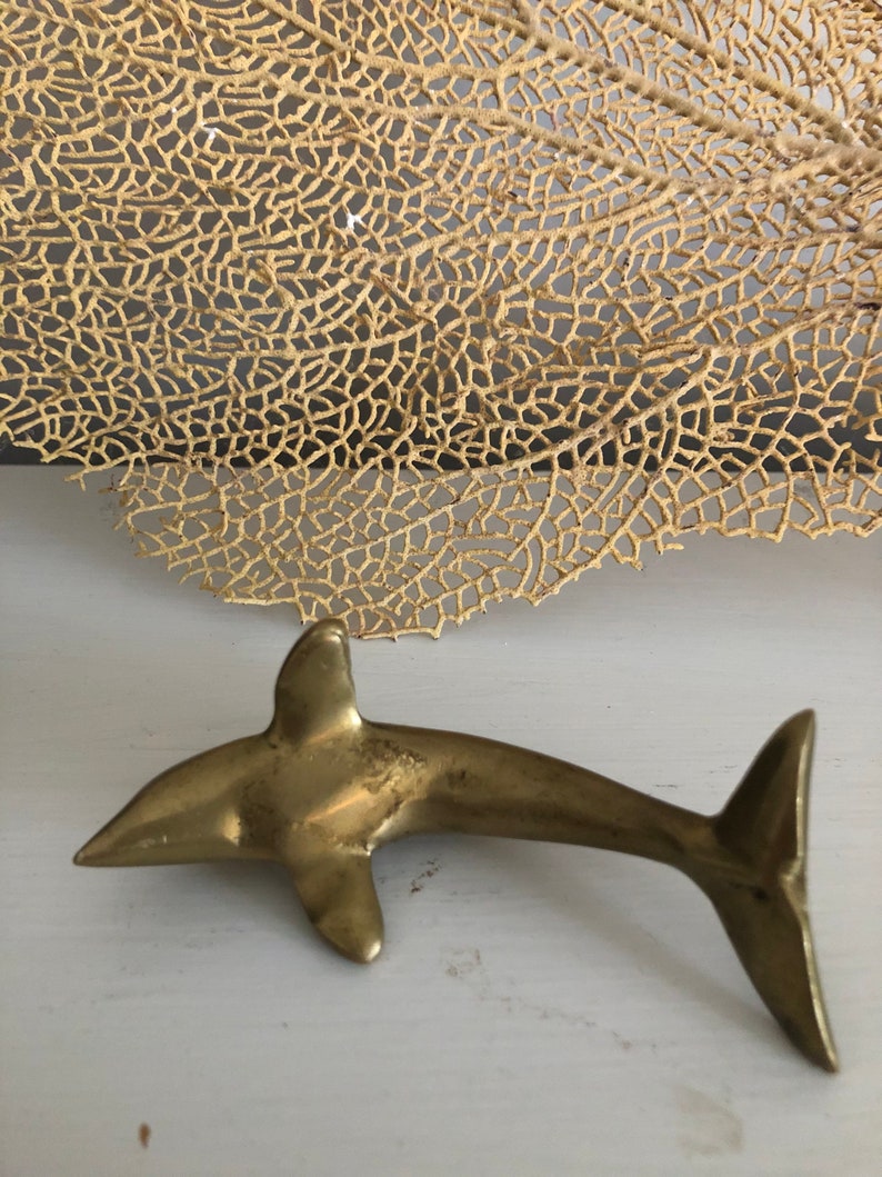 May include: A gold-colored metal dolphin figurine. The dolphin is in a swimming pose with its tail raised.