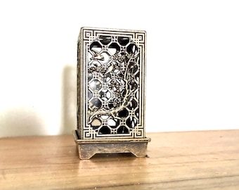 May include: A rectangular bronze-toned metal lantern featuring an intricate openwork lattice pattern. The front panel displays a raised relief design of a flowering branch with small birds. The structure sits on a matching square base.