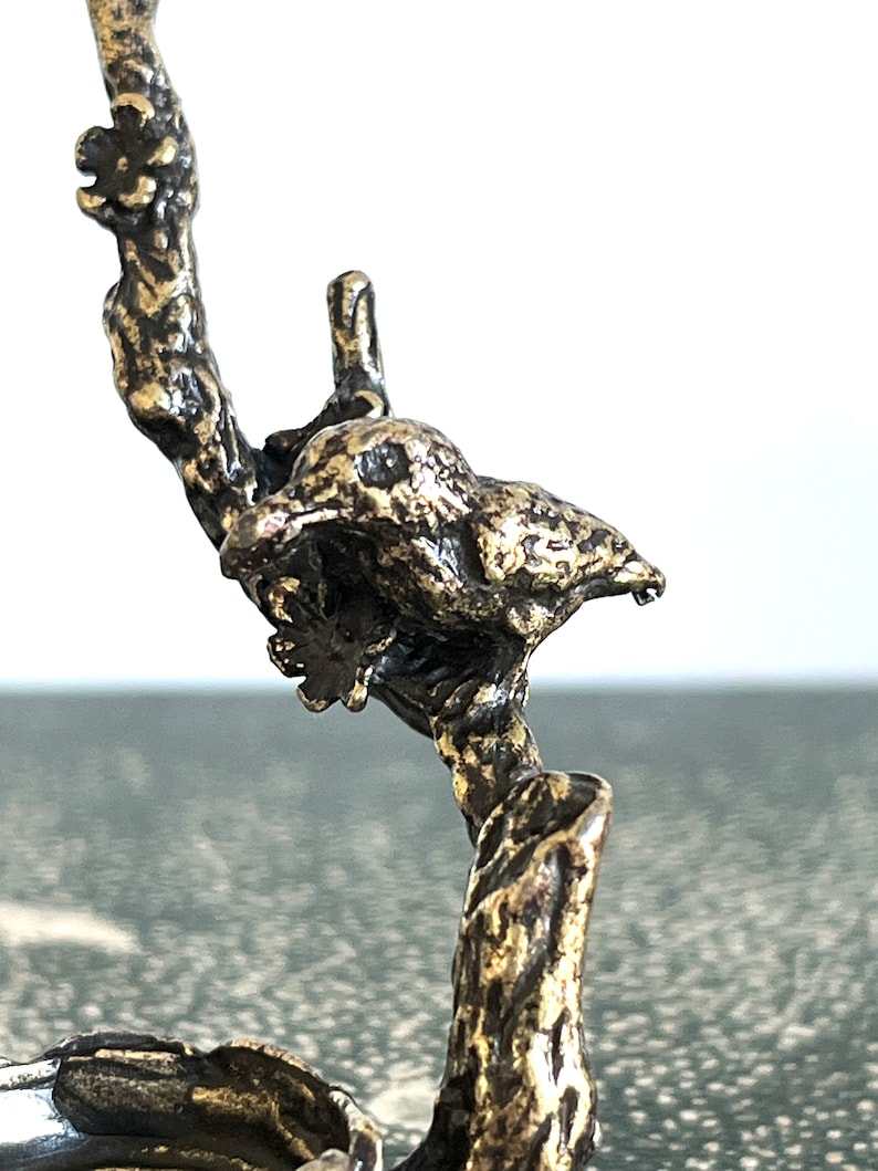 May include: A gold-toned metal bird perched on a branch, the bird is facing right and has a detailed, textured surface.