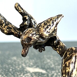 May include: Close-up of a bronze sculpture of a creature with a long neck and a head that resembles a bird. The sculpture is detailed and textured, with a gold-like finish.