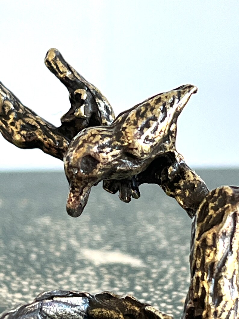 May include: Close-up of a bronze sculpture of a creature with a long neck and a head that resembles a bird. The sculpture is detailed and textured, with a gold-like finish.