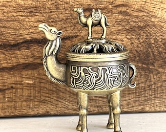 May include: A detailed brass camel incense burner. The burner features a large camel base with intricate etched patterns and a smaller camel figure on top. The design includes a pierced lid for releasing incense smoke.