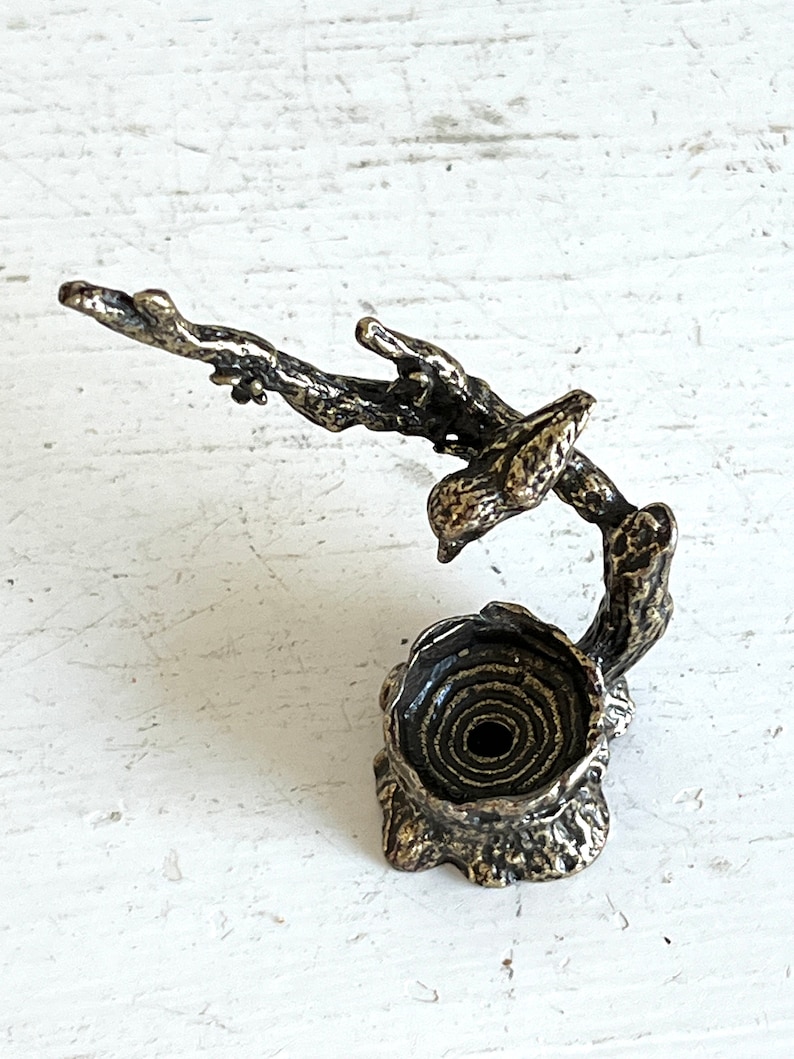 May include: A bronze sculpture of a bird perched on a branch with a nest at the base. The sculpture is detailed with textured bark and a spiral-shaped nest.
