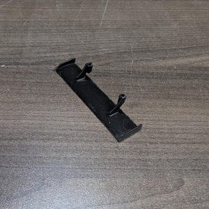 May include: A small, black plastic spoiler with two vertical posts. The spoiler is rectangular with a slightly curved top and bottom edge. The object is likely a model car accessory.