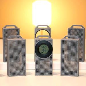 May include: A collection of gray, rectangular, perforated speakers with handles. One speaker has a digital display showing temperature and humidity readings. The speakers are arranged on a white surface against a warm, yellow background.