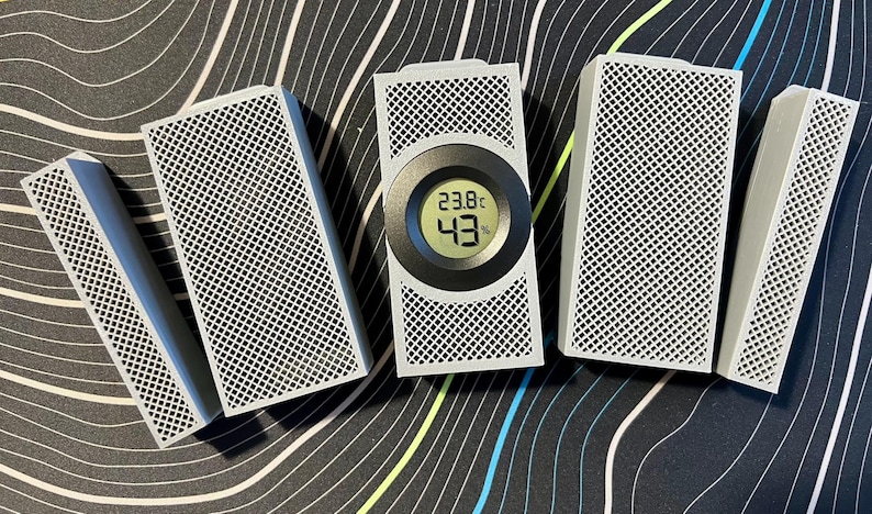 May include: A collection of white rectangular devices with a grid pattern, some with a blue accent. One device has a digital display showing 23.8&deg;C and 43%. The devices are arranged on a patterned surface.
