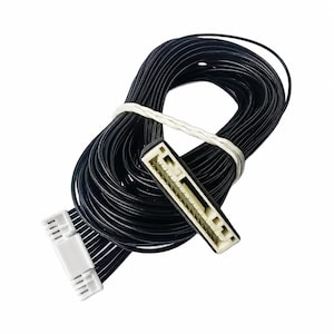 May include: A coiled bundle of thin black electrical wires secured with a white tie. The cable features a white plastic multi-pin connector at one end and a larger, rectangular white plastic interface port at the other end with visible metal pins.
