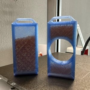 May include: Two blue rectangular 3D-printed objects with a handle at the top. One is solid, the other has a large circular cutout. Both have a brown, textured interior and a lattice-like exterior.