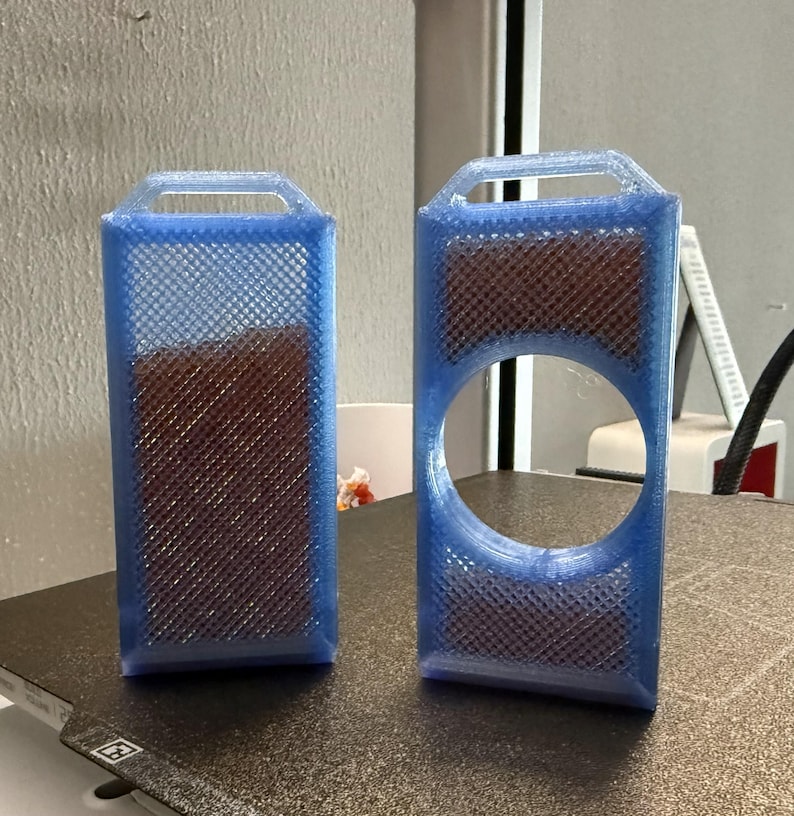 May include: Two blue rectangular 3D-printed objects with a handle at the top. One is solid, the other has a large circular cutout. Both have a brown, textured interior and a lattice-like exterior.