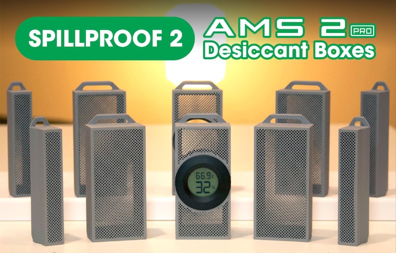 May include: A collection of gray desiccant boxes with perforated sides and handles. One box features a digital display showing temperature and humidity. The text "SPILLPROOF 2" and "AMS 2 PRO Desiccant Boxes" are displayed in green and white.