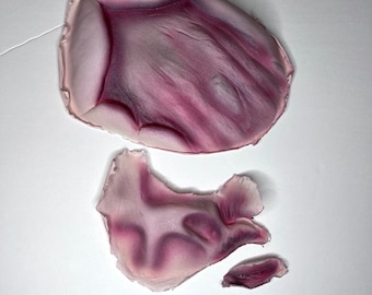 May include: Three pieces of purple and white silicone mold for making fake wounds. The molds are shaped like a hand, a finger, and a small piece of skin.
