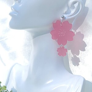 May include: Pink cherry blossom earrings with a silver hook. The earrings are made of acrylic and have a delicate, feminine look.