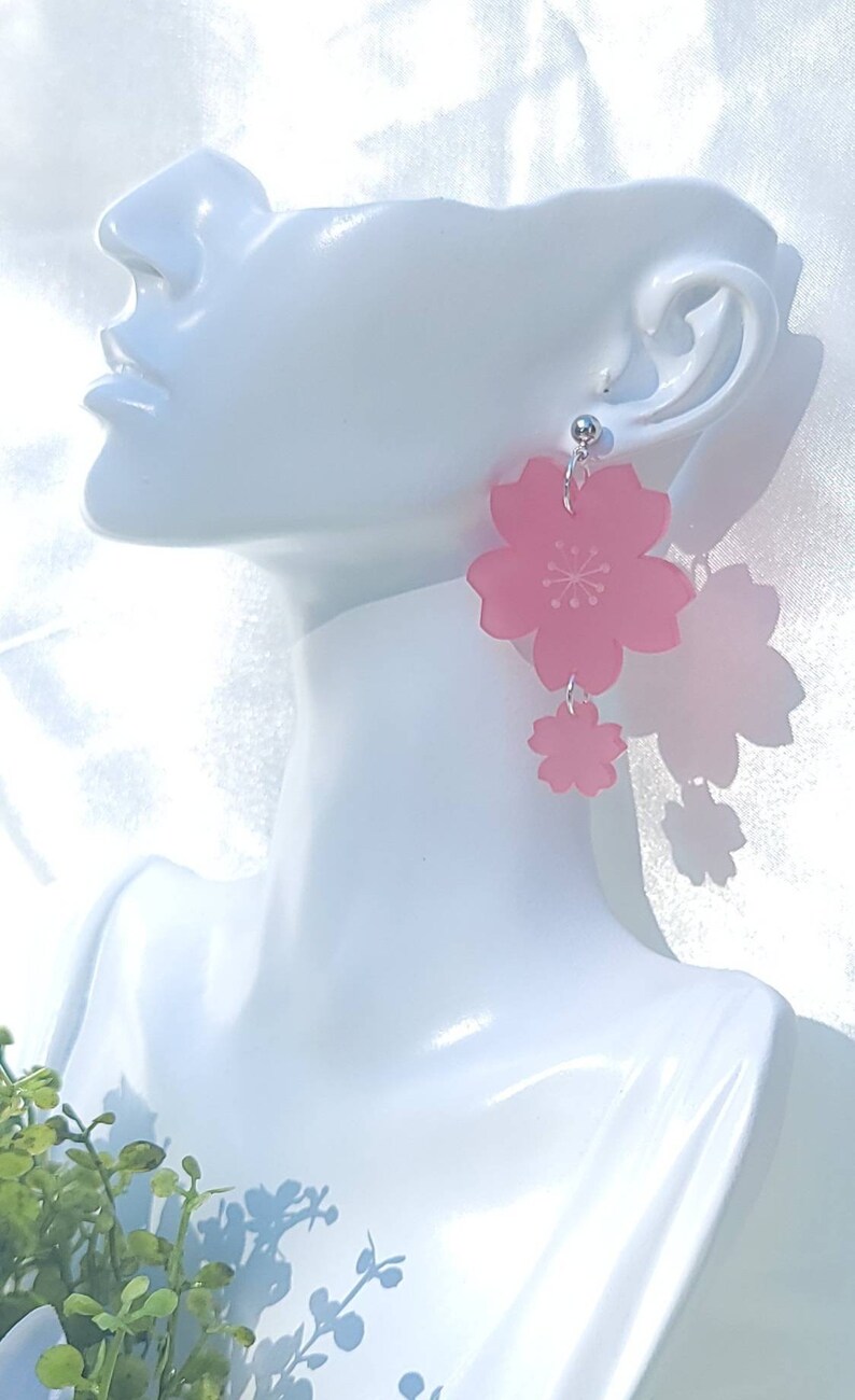 May include: Pink cherry blossom earrings with a silver hook. The earrings are made of acrylic and have a delicate, feminine look.