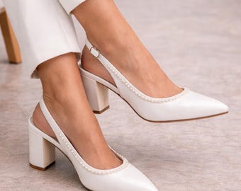 May include: White slingback heels with a pointed toe and block heel. The shoes are adorned with a delicate pearl trim along the topline and slingback strap. The heels are approximately 2.5 inches high.