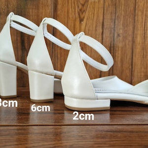 May include: Three pairs of white heeled sandals with ankle straps. The heels are 8 cm, 6 cm, and 2 cm tall.