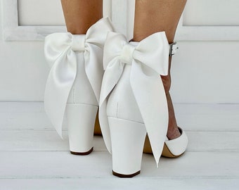 Può includere: Tacchi da sposa in raso bianco con un grande fiocco sul retro di ogni scarpa.
