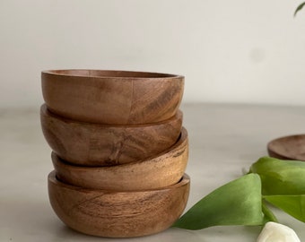 May include: A stack of four small, wooden bowls. The bowls are a light brown color and have a smooth, rounded shape. The bowls are stacked on top of each other, with the largest bowl on the bottom and the smallest bowl on top.