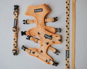 May include: A set of dog accessories in a yellow and black bee pattern. The set includes a harness, a collar, and a leash. The harness has a honeycomb pattern with bees, while the collar and leash have a smaller bee pattern. The accessories are all made of a soft, comfortable material and are perfect for everyday use.