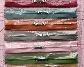 May include: A package of colorful zippers in various shades, including red, green, orange, gray, pink, olive, yellow, and blue. Each zipper is individually packaged and features a silver metal pull. The package header reads "Happy Zippers 2".