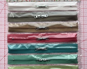 May include: A package of eight 16-inch zippers in various colors, including white, gray, brown, red, teal, green, and light blue. The package is labeled "Happy Zippers 3" and includes text from "Lori Holt of Bee in my Bonnet."