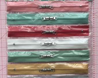 May include: A package of Happy Zippers in various colors, including pink, teal, red, white, green, gold, gray, and turquoise. Each zipper is individually packaged and features a silver metal pull. The packaging has a sewing machine pattern and the text "Happy Zippers".