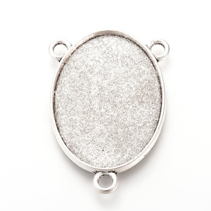 May include: Oval-shaped silver-toned pendant base with three loops for attaching to a chain or other jewelry components. The center has a textured surface, ready for embellishment. Ideal for DIY jewelry projects.