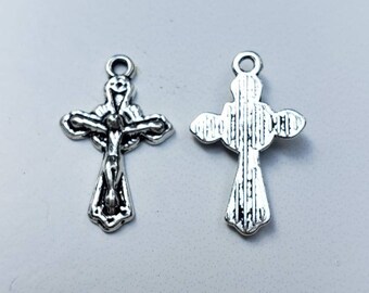 May include: Two silver-colored crucifix charms. One charm shows a detailed depiction of Jesus on the cross, while the other displays the back of the cross with vertical lines. Both charms have a small loop at the top for hanging.