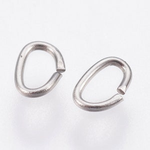 May include: Two silver-colored, oval-shaped jump rings with open ends, set against a white background. The rings are made of a shiny, metallic material, and are likely used for jewelry making or crafts.