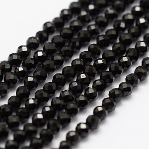May include: Strands of faceted black beads, likely gemstones or glass, are arranged closely together. The beads have a glossy finish and reflect light, creating a sparkling effect. The beads are strung together, suggesting they are for jewelry making or crafting.