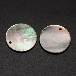 May include: Two round, iridescent mother-of-pearl beads with a hole drilled through each. The beads have a pearlescent sheen with hints of pink, green, and gray. The background is a dark gray.