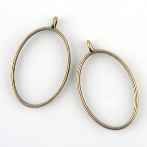 May include: Two antique brass-colored oval pendant frames with a small loop at the top. The frames are empty, with a simple, minimalist design. These frames are ideal for jewelry making and crafting.