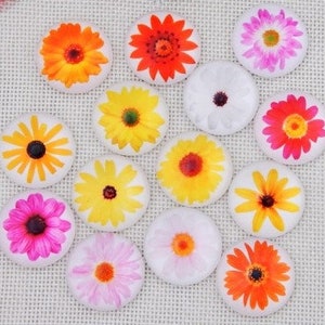 May include: A collection of round, floral-themed decorative objects. The objects feature vibrant gerbera daisy designs in shades of orange, red, yellow, pink, and white. The daisies have detailed petals and dark centers, set against a white background.