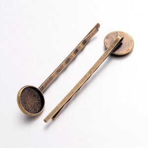 May include: Two antique bronze-colored bobby pins. One pin features a small, round, flat bezel. The other pin is a simple, textured design. These hair accessories are ideal for adding a vintage touch to any hairstyle.