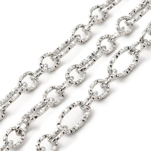 May include: Close-up of three silver-colored chain necklaces. The chains have an oval link design with a textured, hammered appearance. The chains are arranged diagonally against a white background, showcasing the jewelry's details.