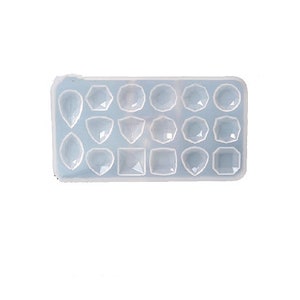 May include: A light blue silicone mold with various gemstone shapes. The mold features a variety of geometric designs, including teardrops, hexagons, and squares. The mold is designed for crafting resin jewelry or decorative elements.