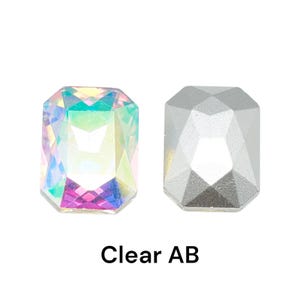 May include: Two faceted, rectangular rhinestones. One is clear with an iridescent, rainbow-like finish, and the other is a solid, silvery-gray color. The text "Clear AB" is printed below the rhinestones.