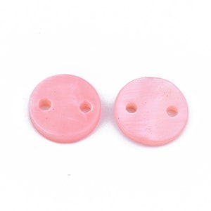 May include: Two round, light pink buttons with two holes each. The buttons have a slightly marbled appearance and are set against a white background. These buttons are suitable for sewing and craft projects.